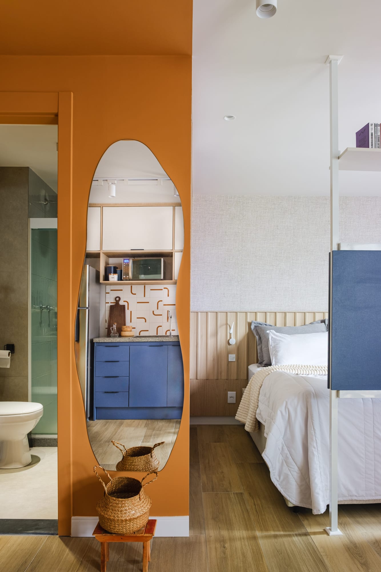 Organic mirror on the mustard wall reflecting the kitchen, between the bathroom and the apartment bed.