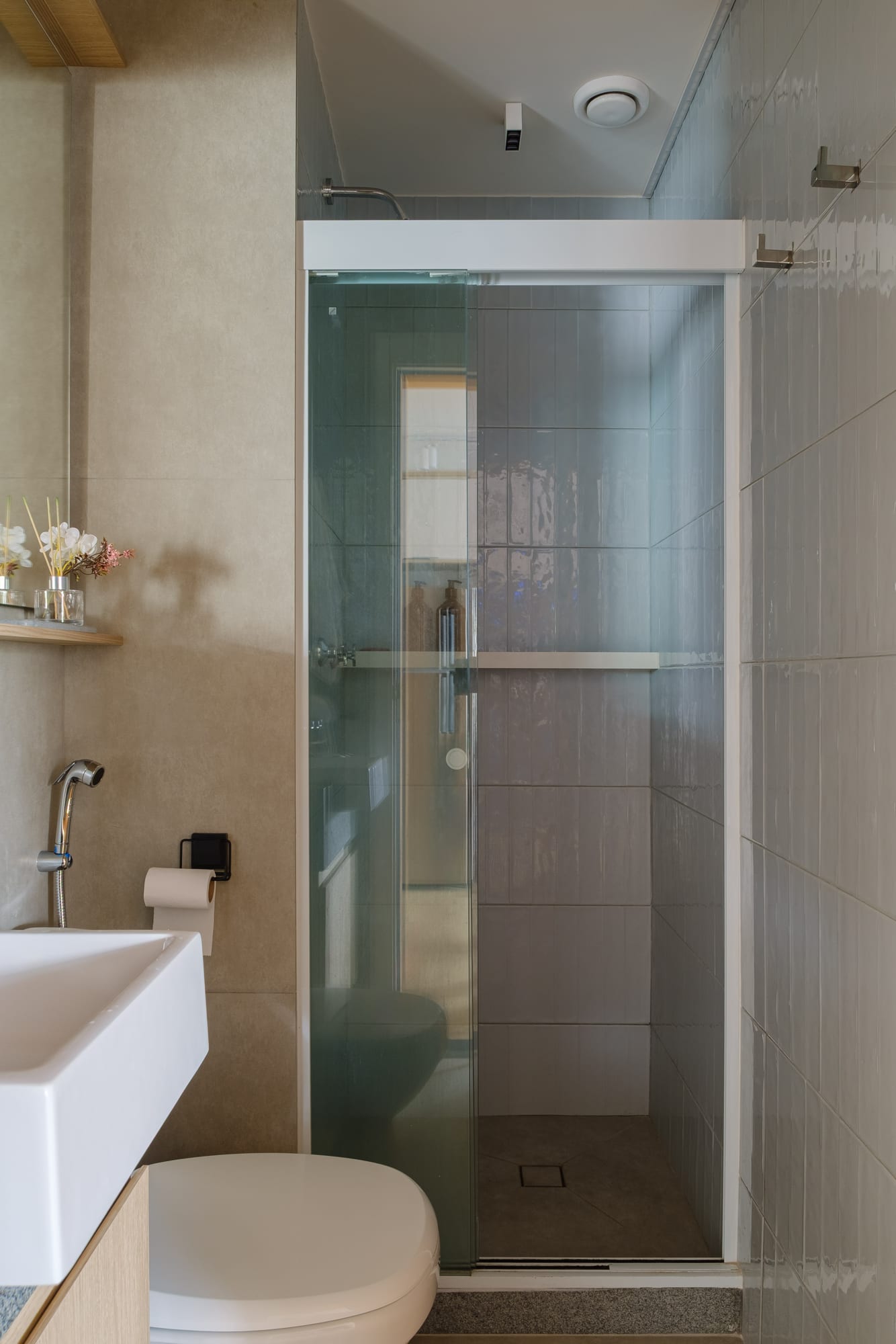 Bathroom with a glass shower enclosure, blue-gray tile, white sink on a granite countertop and toilet.
