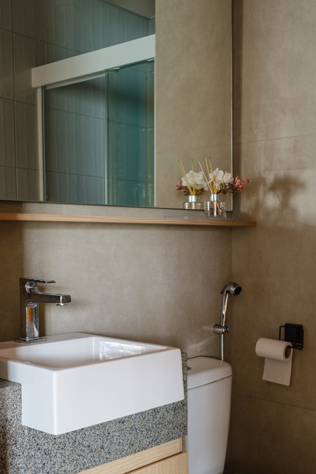 Bathroom counter detail with a white sink, chrome faucet, mirror and reed diffusers on the shelf.