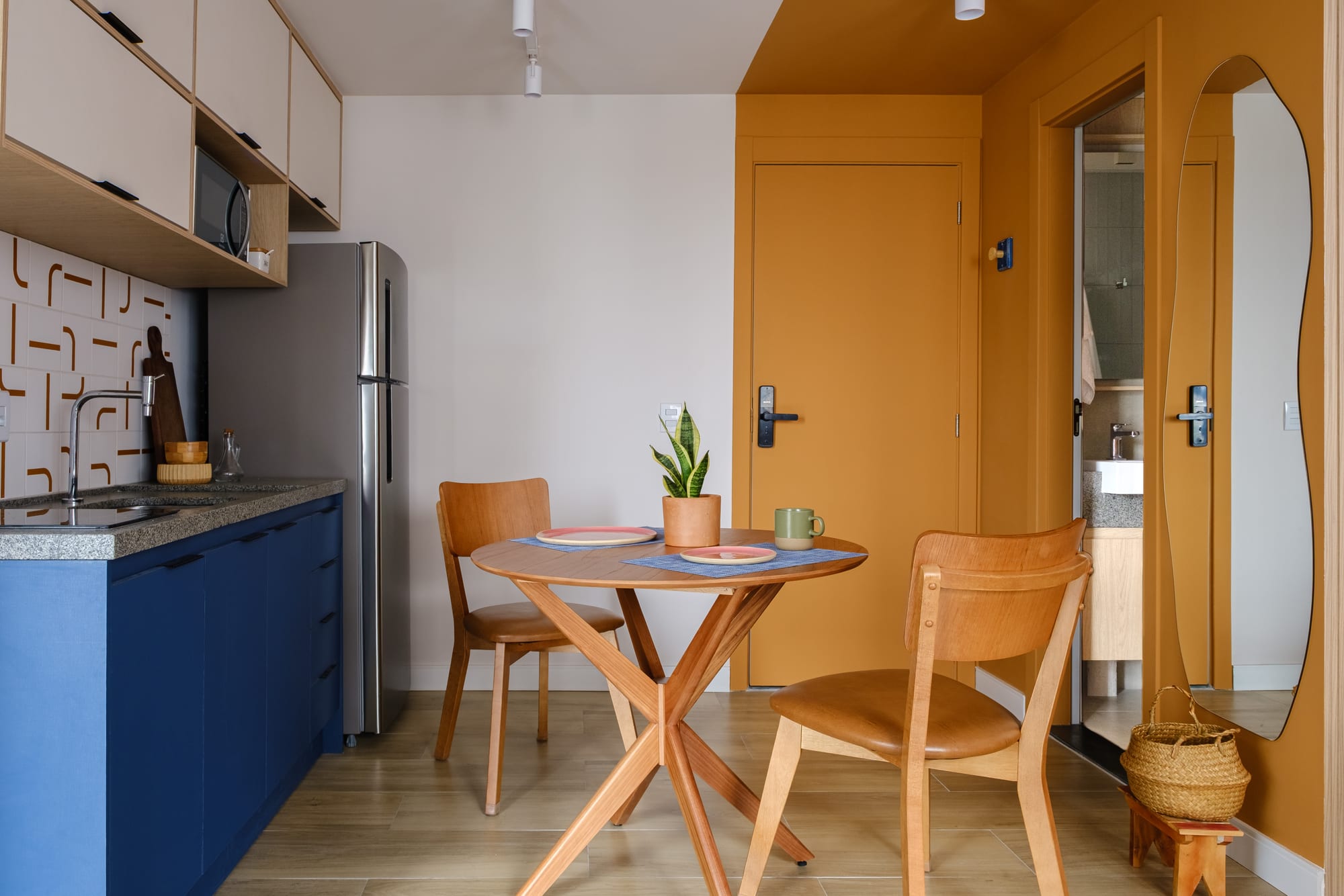 Overview of the blue kitchen integrated with the round dining table, mustard entry door and organic mirror.