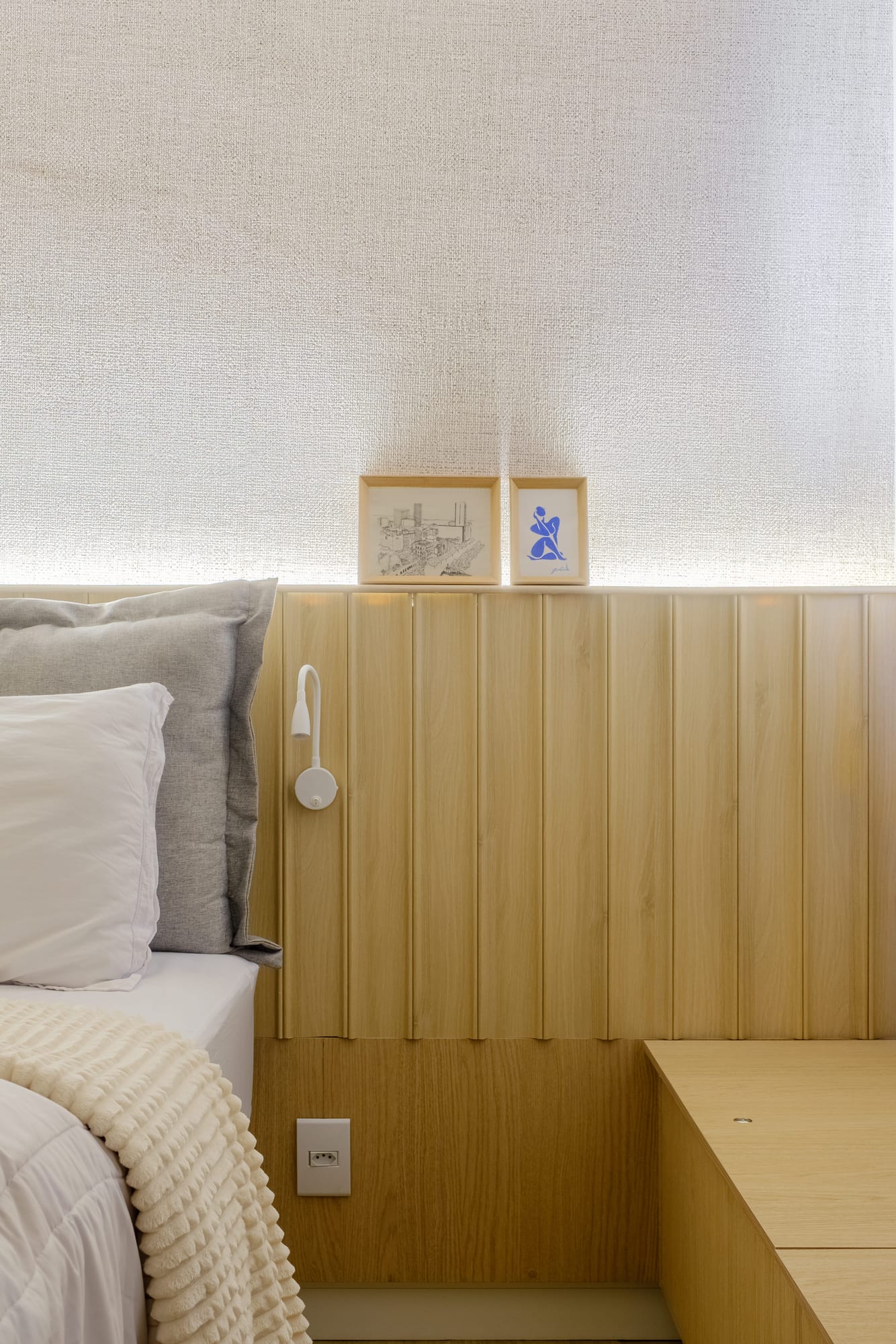 Wooden headboard with built-in lighting, decorative frames, a white reading lamp and a light-wood storage bench.