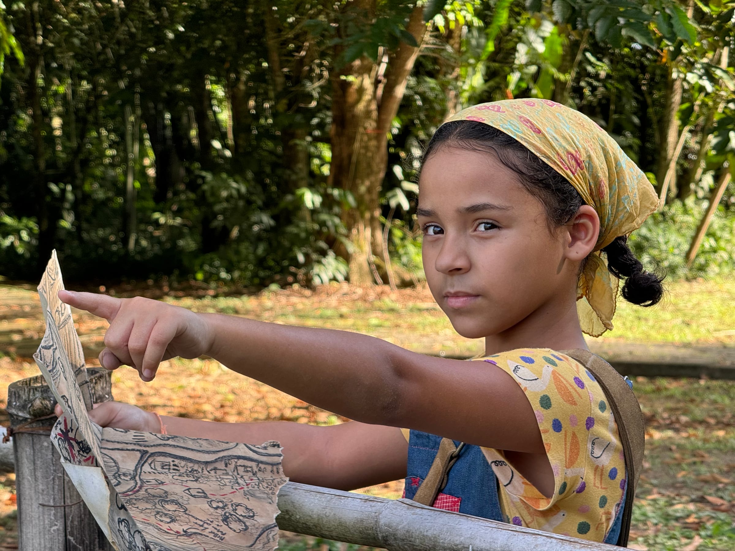 Lara Reis como Pipa segura um mapa e aponta o caminho em uma área arborizada