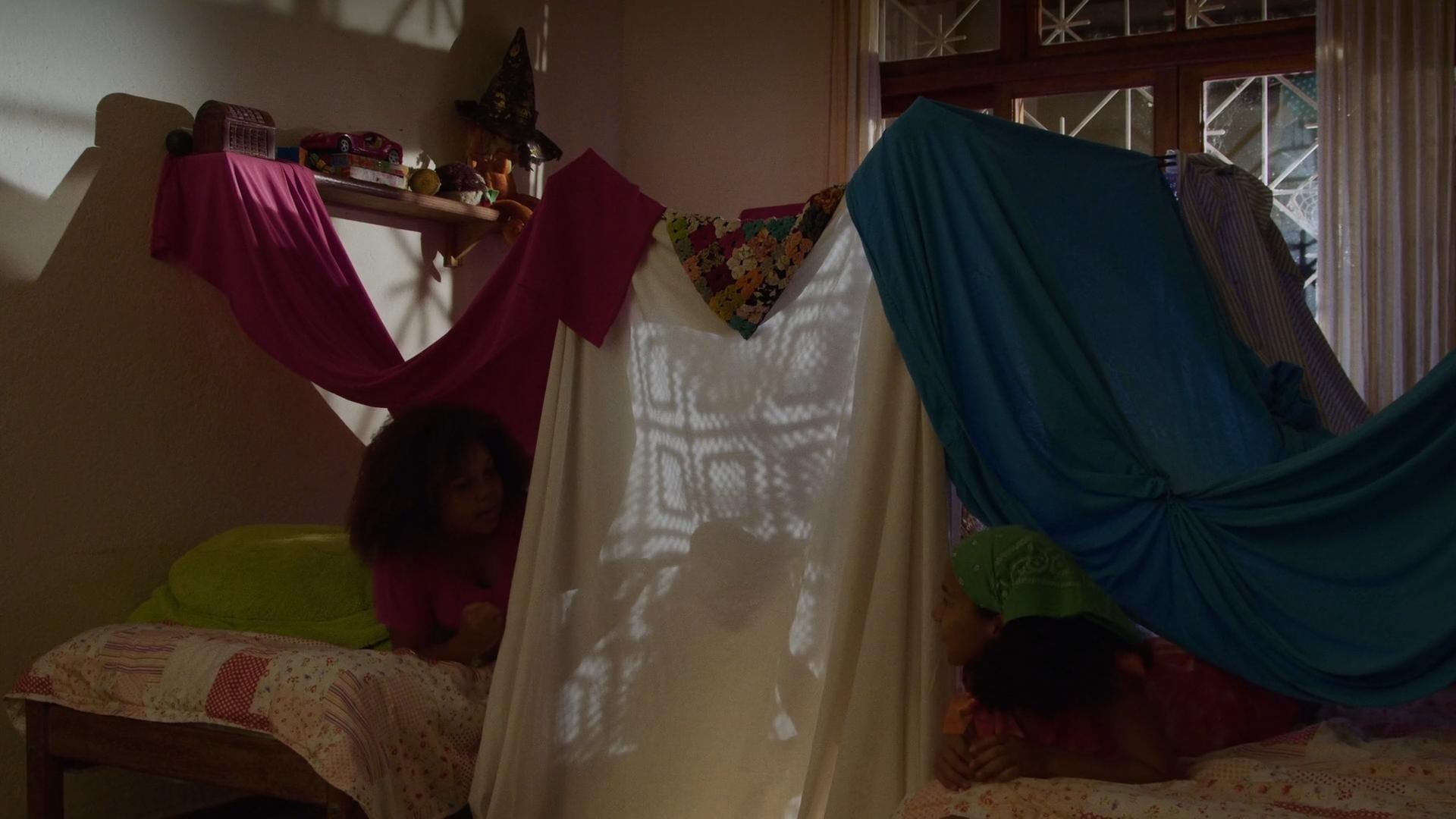 Crianças brincam em uma cabana de tecidos dentro de um quarto